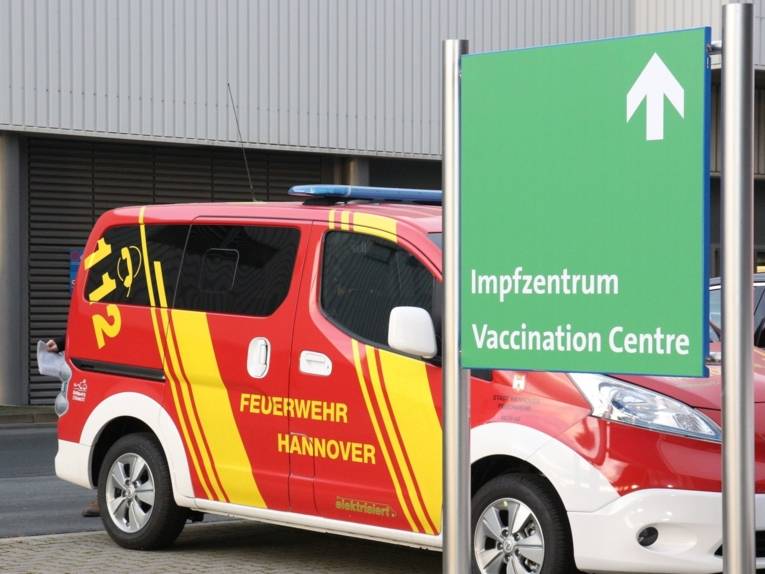 Schild mit der Aufschrift "Impfzentrum", dahinter ein Fahrzeug der Feuerwehr Hannover